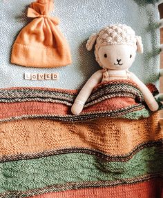 a stuffed animal laying on top of a blanket next to a hat and bag with the word loved written on it