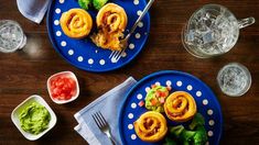 two blue plates with food on them next to glasses and silverware, one has broccoli