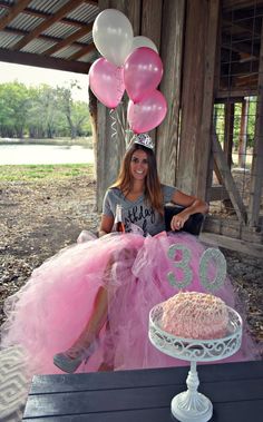 a woman sitting in front of a cake with balloons on it and a birthday hat