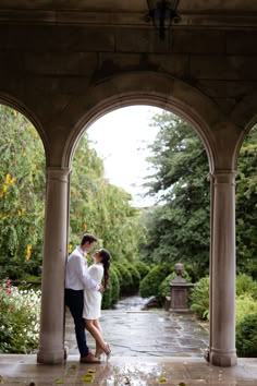 a man and woman are standing under an archway in the rain with their arms around each other