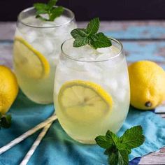 two glasses filled with lemonade on top of a blue cloth next to strawberries