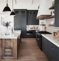 a large kitchen with black cabinets and white counter tops, wood flooring and pendant lights hanging from the ceiling