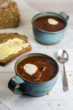 two mugs of soup with bread and butter on the side next to each other