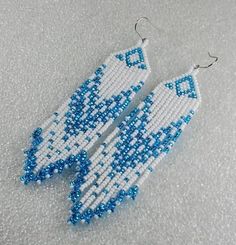 a pair of beaded earrings with blue and white beads hanging from it's sides