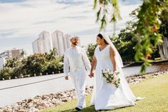 a bride and groom are walking along the grass by the water in their wedding attire