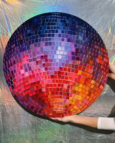 a woman holding a colorful mosaic plate in front of a wall covered with holographics