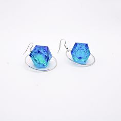 This listing is for a pair of lightweight silver hoops with D20 dice suspended in the middle. The ear wire's are silver plated and come with earring backs to keep them from slipping out. The dice themselves are D20 (twenty sided dice) that are un-inked. They are made from blue and green resin from another project so these will likely be a one-of-a-kind. Drop length: 1.5 Inches Dice height: .75 Inches Silver Plated Each piece is a one of a kind and unique, if you have any questions please don't hesitate to reach out! Packaging: Items will come packaged in a small pillow box for safe transportation and can also be used as it's own gift wrapping. Note that I work towards using recyclable materials whenever possible. Depending on your monitor settings the item may look slightly different due t Cheap Novelty Blue Earrings, Quirky Blue Earrings For Gift, Dnd Dice Necklace, 20 Sided Dice Earrings, Nerd Jewelry, Blue Artsy Resin Earrings, D20 Dice, Small Pillows, Pillow Box