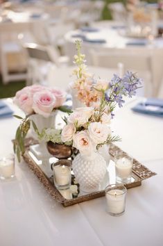 a tray with flowers and candles on top of a white table cloth covered dining room