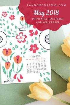 a calendar with flowers on it next to yellow tulips and a green envelope