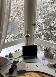 a laptop computer sitting on top of a desk next to a window covered in snow