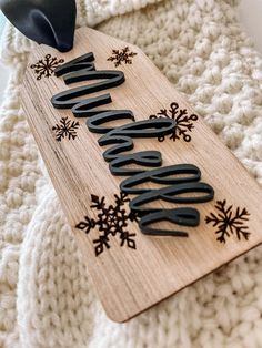 a wooden sign sitting on top of a white blanket next to a black hat and snowflakes