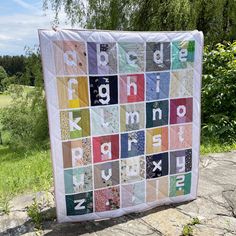 a baby quilt with letters on it sitting in front of some grass and trees,