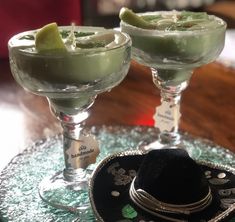 two margaritas are sitting on a glass plate with a cowboy hat next to them