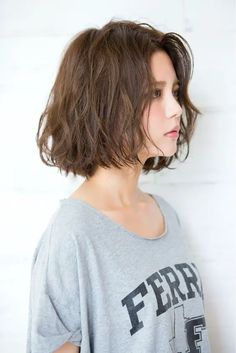 a woman with short brown hair wearing a gray shirt and standing in front of a white wall