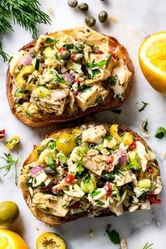 two pieces of bread with chicken salad on them next to lemons and olives