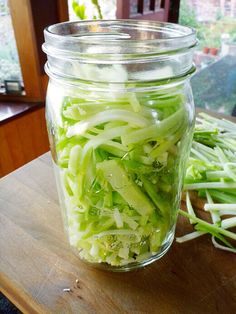 a glass jar filled with sliced green onions on top of a wooden table next to a window