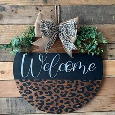 a leopard print welcome sign hanging on a wooden wall with a bow and ribbon attached to it