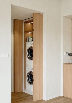 a washer and dryer in a room with white walls, wood floors and cabinets