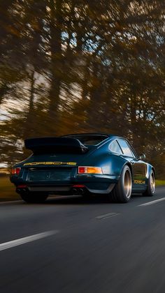 the rear end of a blue sports car driving down a road with trees in the background