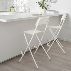 two white folding chairs sitting in front of a kitchen counter with a clock on the wall