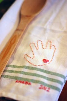 a wooden spoon sitting on top of a table next to a white napkin with a hand embroidered onto it