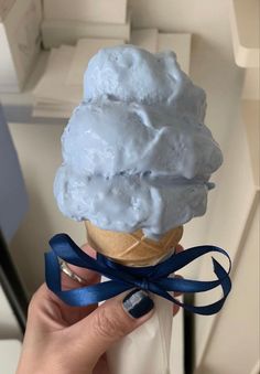 a hand holding an ice cream cone with blue ribbon around it and white icing on top