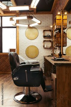 a barber chair in front of a brick wall with round lights hanging from it's ceiling