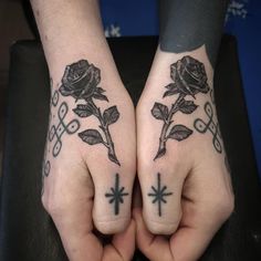 two hands with tattoos and crosses on them, both holding roses in the middle of their fingers