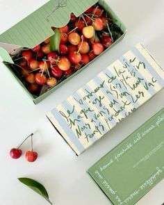 some cherries are in a green box on a table next to a notepad