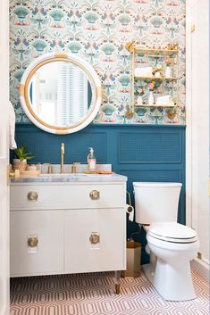 a white toilet sitting next to a bathroom sink under a round mirror on top of a wooden cabinet