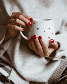 a woman with red nails holding a white coffee cup