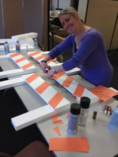 a woman sitting at a table with orange and white strips on it, making an art project