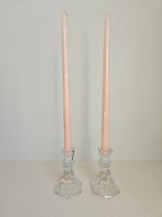 two pink candles sitting next to each other on top of a white table with a wall in the background