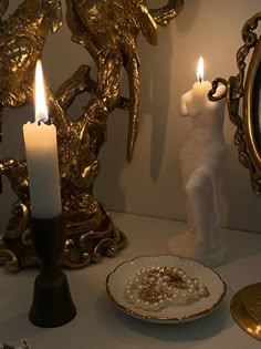 two candles are lit on a table next to a plate with a ring in it