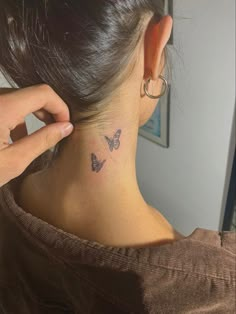 a woman with a small butterfly tattoo on her neck and behind her ear, looking at the mirror