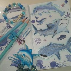 an open notebook with dolphin drawings and pencils on the cover, along with other items