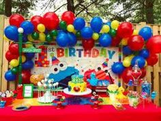 a birthday party with balloons, cake and decorations on a table in front of a wooden fence