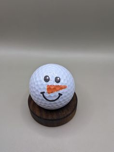 a golf ball with a face painted on it sitting on a wooden stand in front of a white background