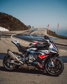 a red, white and blue motorcycle parked on the side of a road next to a mountain