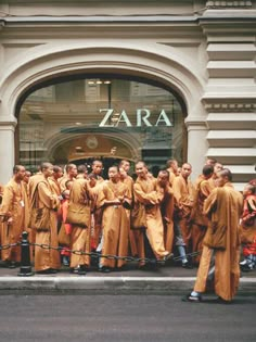 a group of people in orange robes standing on the side of a street next to a building