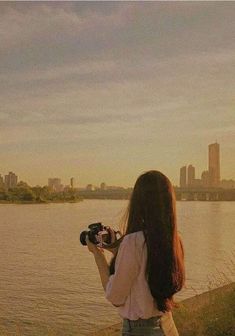 a woman standing next to a body of water with a camera in front of her