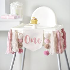 a one year birthday banner hanging from a chair with tassels and pom poms