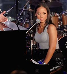 a woman sitting in front of a microphone next to a piano and drum set on stage