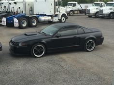 a black sports car parked in a parking lot next to other cars and semi trucks