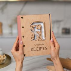 two hands holding up a wooden recipe book with the letter f on it, and another person's hand reaching for one