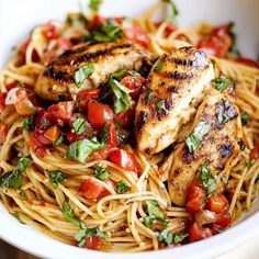 a white bowl filled with pasta and chicken topped with tomatoes, parsley and basil