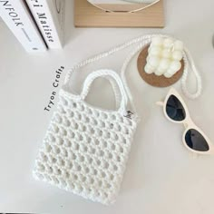 a white crochet bag sitting on top of a table next to sunglasses and a book