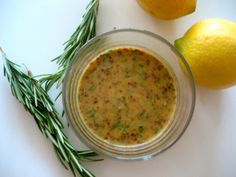 a glass bowl filled with food next to two lemons and a rosemary sprig