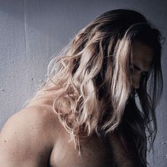 a man with long hair standing in front of a gray wall and looking off to the side