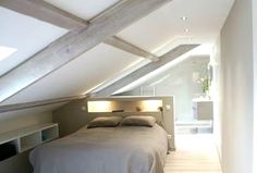 a bed sitting in the middle of a bedroom under a slanted roof over a bathroom